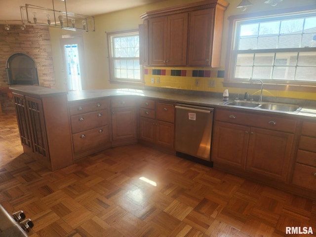 kitchen featuring dishwasher, a peninsula, brown cabinets, and a sink