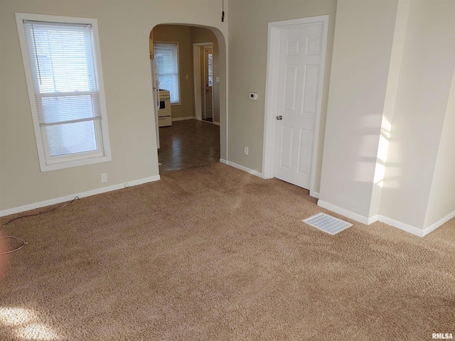 carpeted empty room featuring visible vents, arched walkways, and baseboards