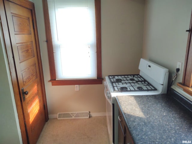 kitchen featuring white gas stove, baseboards, visible vents, and light tile patterned flooring