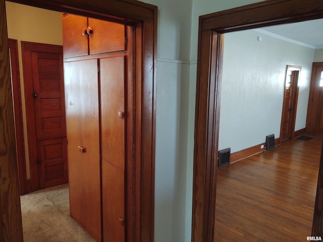 corridor featuring baseboards, wood finished floors, visible vents, and ornamental molding