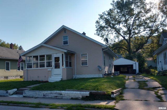 bungalow-style home with a detached garage, entry steps, a front yard, an outdoor structure, and a sunroom