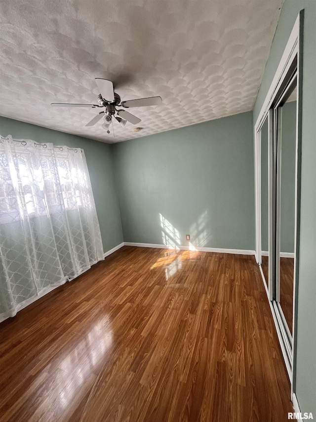 unfurnished bedroom with wood finished floors, baseboards, ceiling fan, a closet, and a textured ceiling