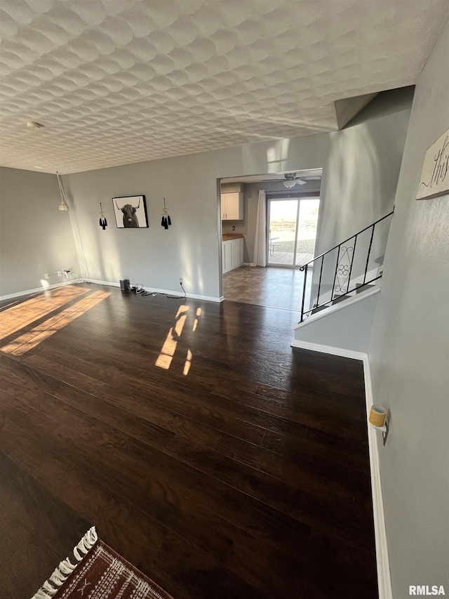 unfurnished living room featuring a textured ceiling, a ceiling fan, baseboards, and wood finished floors