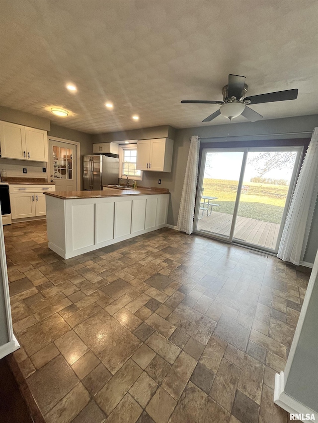 kitchen with a peninsula, white cabinets, freestanding refrigerator, and a sink