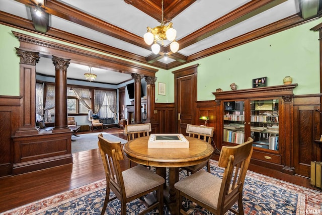 dining room with a notable chandelier, wood finished floors, crown molding, wainscoting, and ornate columns