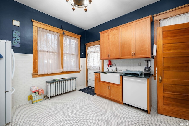 kitchen with white appliances, a wainscoted wall, radiator heating unit, a sink, and dark countertops