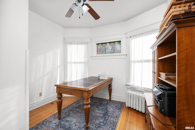 office area featuring a ceiling fan, baseboards, light wood-style floors, and radiator heating unit