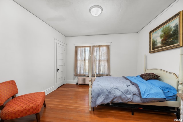 bedroom featuring radiator heating unit, baseboards, and wood finished floors