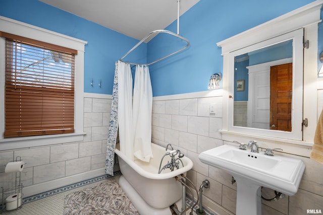 full bathroom with a shower with shower curtain, a wainscoted wall, a soaking tub, a sink, and tile walls