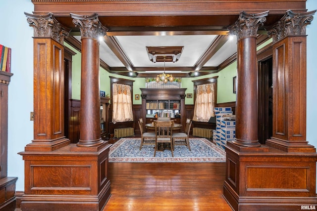 dining room featuring a wainscoted wall, beam ceiling, wood finished floors, radiator heating unit, and decorative columns