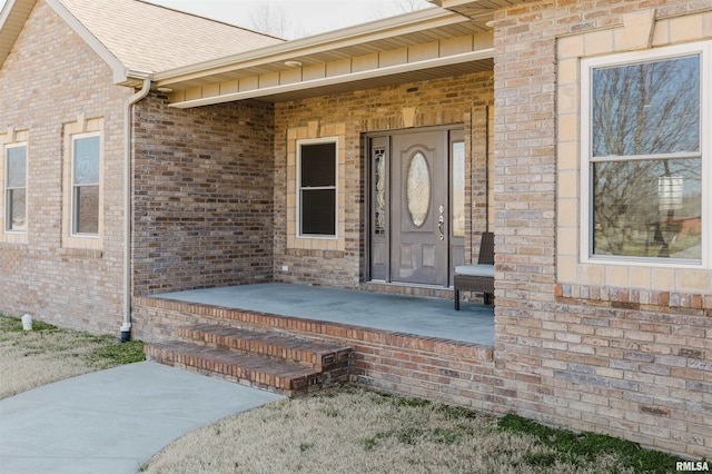 entrance to property with brick siding, covered porch, and a shingled roof