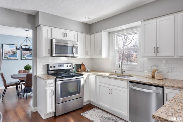 kitchen with a sink, dark wood-type flooring, light stone countertops, and stainless steel appliances