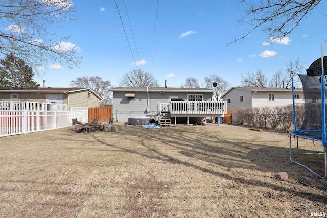 rear view of property with a trampoline, a fenced backyard, a yard, and a wooden deck