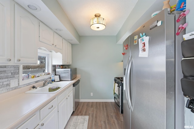 kitchen featuring light wood-type flooring, light countertops, white cabinets, stainless steel appliances, and a sink