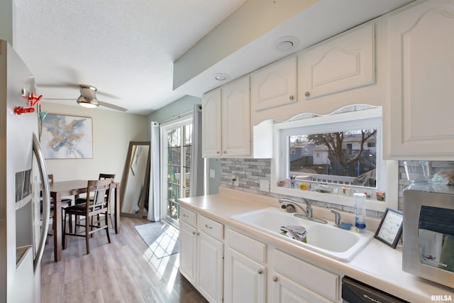 kitchen featuring light wood-style flooring, a sink, decorative backsplash, stainless steel appliances, and white cabinets