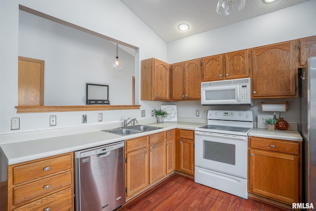 kitchen with brown cabinets, dark wood-type flooring, a sink, stainless steel appliances, and light countertops