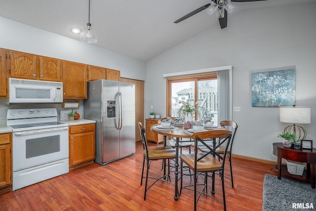 kitchen featuring white appliances, light wood-style floors, brown cabinetry, light countertops, and lofted ceiling