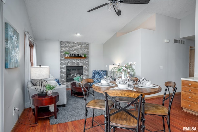 dining area with visible vents, a ceiling fan, wood finished floors, baseboards, and a brick fireplace