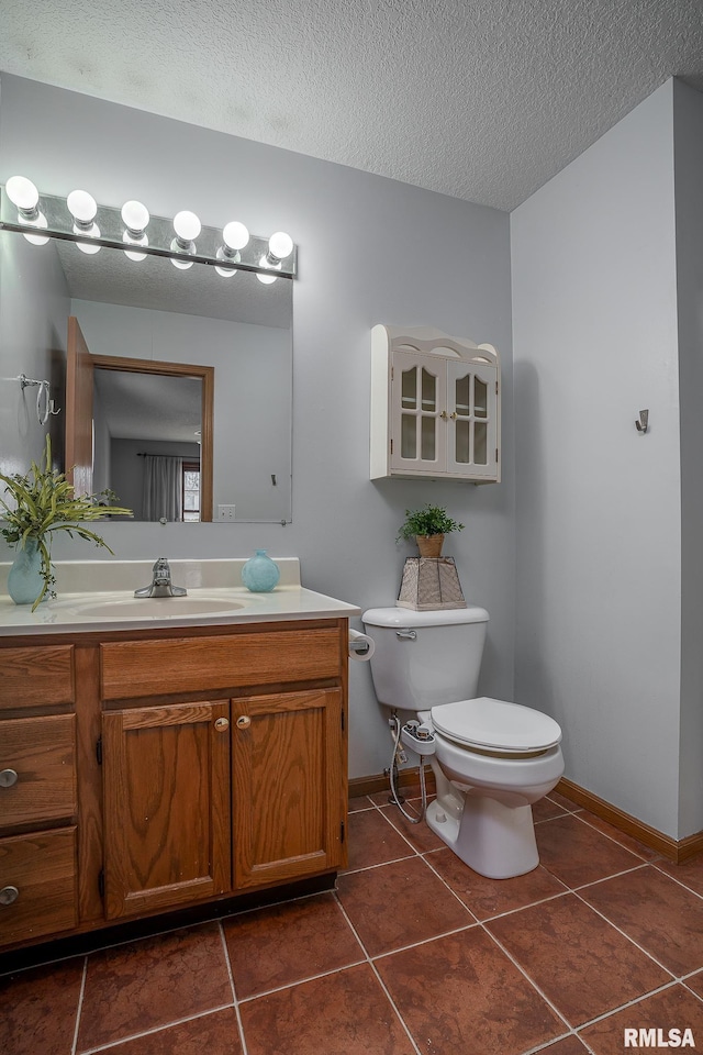 bathroom with tile patterned flooring, baseboards, toilet, vanity, and a textured ceiling