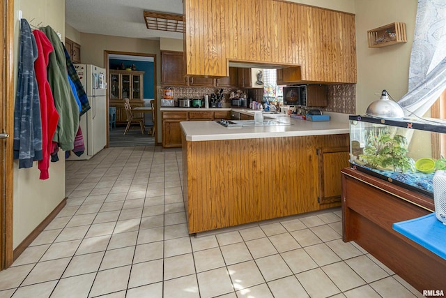 kitchen with light countertops, light tile patterned floors, a peninsula, and freestanding refrigerator