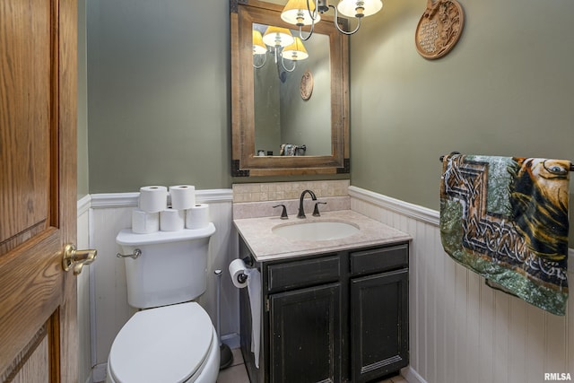 half bathroom with vanity, toilet, and wainscoting