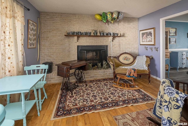 living room featuring a fireplace, brick wall, baseboards, and wood finished floors