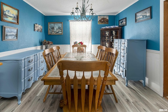 dining area with a wainscoted wall, light wood-style floors, crown molding, and a textured ceiling