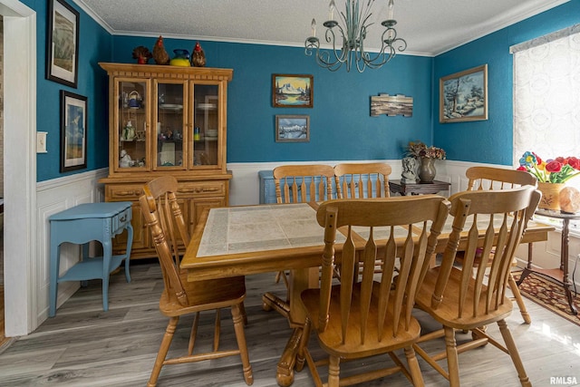 dining space featuring a textured ceiling, light wood-style floors, an inviting chandelier, wainscoting, and crown molding