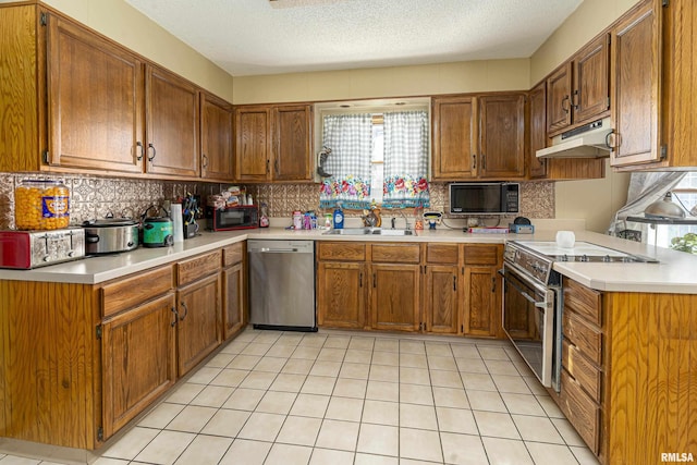 kitchen with under cabinet range hood, a sink, tasteful backsplash, appliances with stainless steel finishes, and light countertops