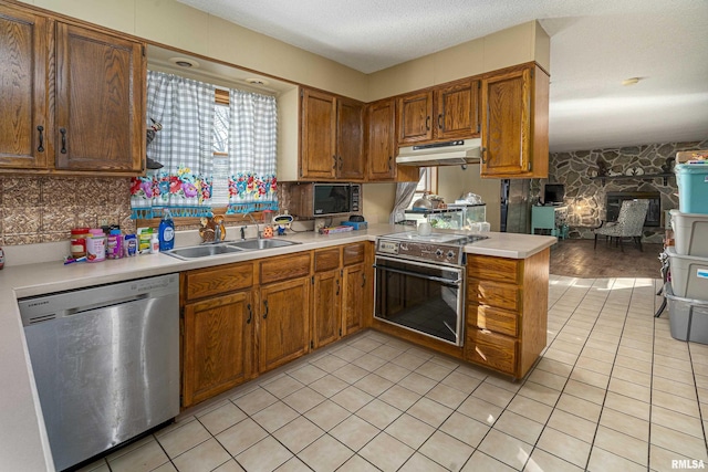 kitchen with a sink, light countertops, under cabinet range hood, appliances with stainless steel finishes, and brown cabinets