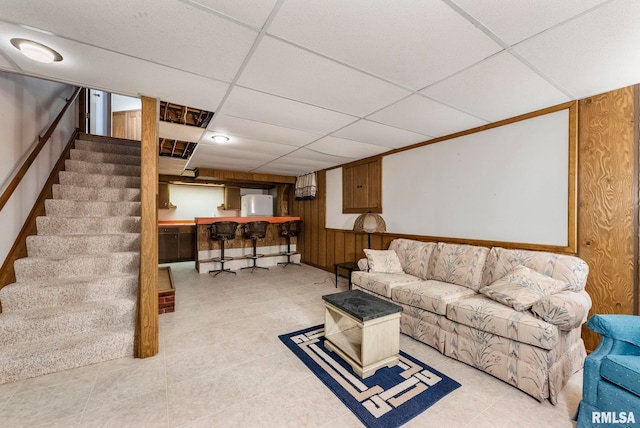 living room with stairway, wooden walls, and a drop ceiling