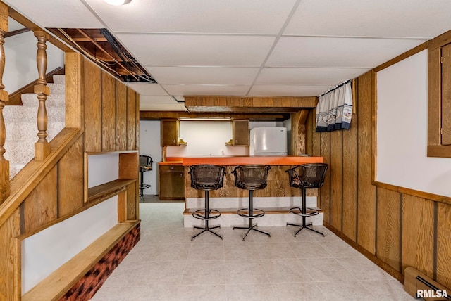 interior space with freestanding refrigerator, stairway, wooden walls, indoor wet bar, and baseboard heating