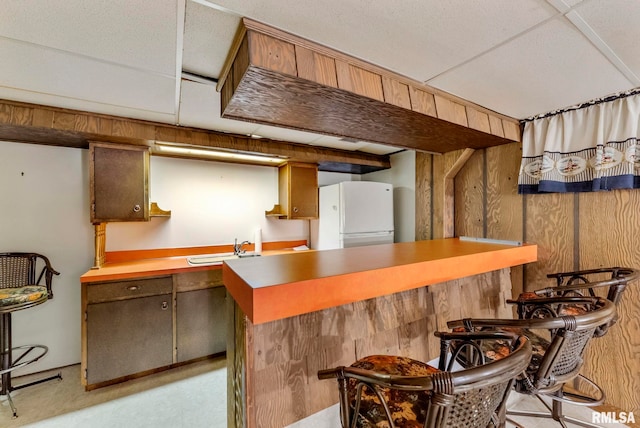 kitchen with wooden walls, a breakfast bar area, light countertops, freestanding refrigerator, and a sink