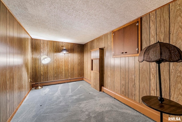 unfurnished room featuring carpet, baseboards, a baseboard radiator, wood walls, and a textured ceiling