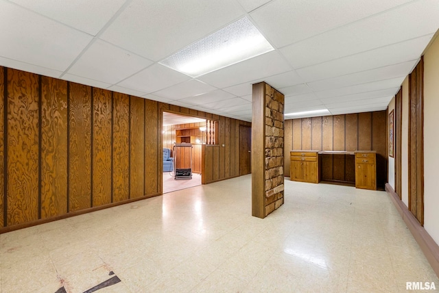 finished below grade area with light floors, a paneled ceiling, and wood walls