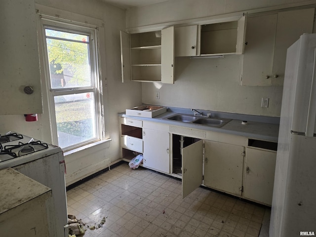 kitchen with open shelves, a sink, freestanding refrigerator, gas range, and light floors