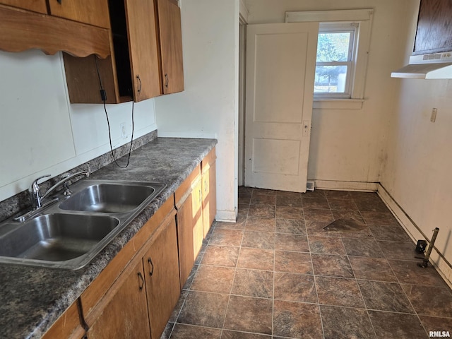 kitchen with dark countertops, brown cabinets, under cabinet range hood, and a sink