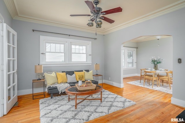 living room with arched walkways, light wood-style flooring, crown molding, and baseboards