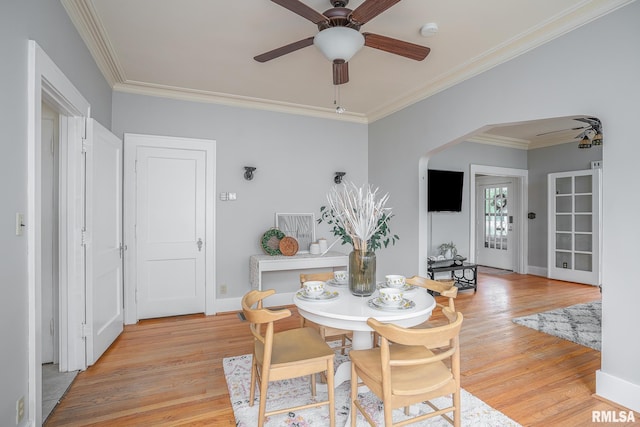 dining space with ceiling fan, arched walkways, light wood-style flooring, and ornamental molding