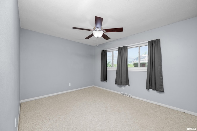 carpeted spare room with visible vents, baseboards, and a ceiling fan