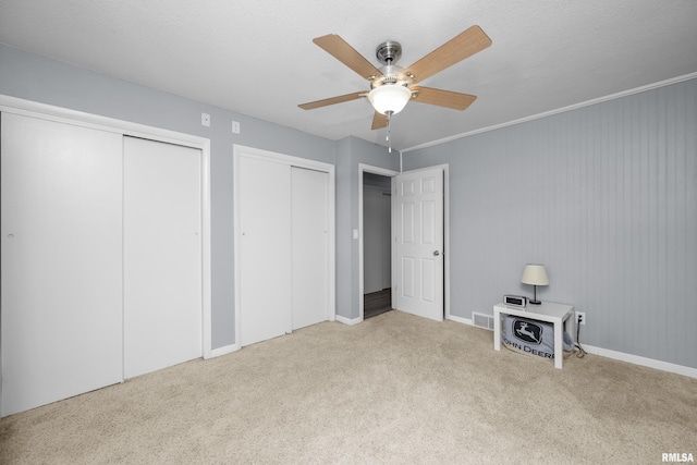 unfurnished bedroom with visible vents, two closets, ceiling fan, carpet, and ornamental molding