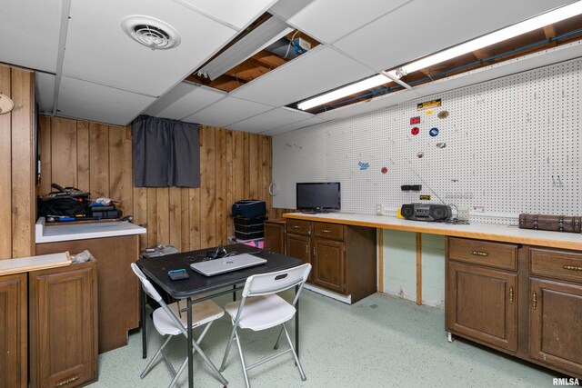 office space with a workshop area, a paneled ceiling, visible vents, and wood walls