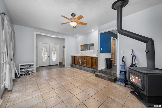 foyer entrance featuring ceiling fan, french doors, a wood stove, light tile patterned flooring, and a textured ceiling