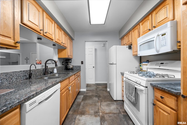 kitchen featuring a sink, dark stone counters, white appliances, and baseboards