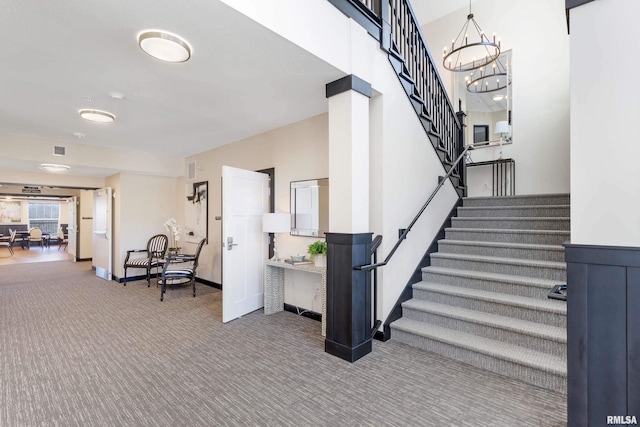 stairs with a notable chandelier, visible vents, baseboards, and carpet floors