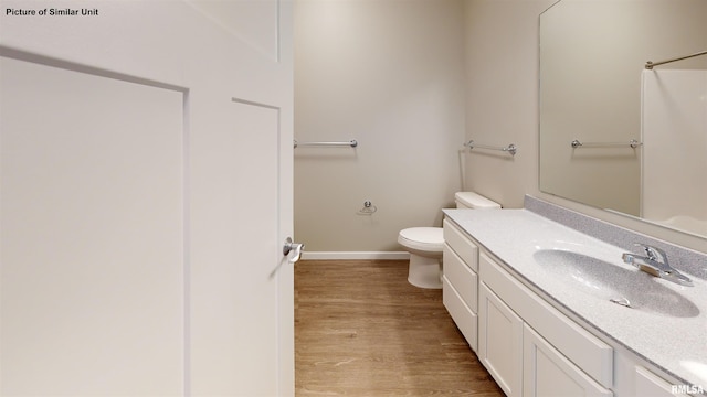 full bath featuring toilet, wood finished floors, baseboards, walk in shower, and vanity