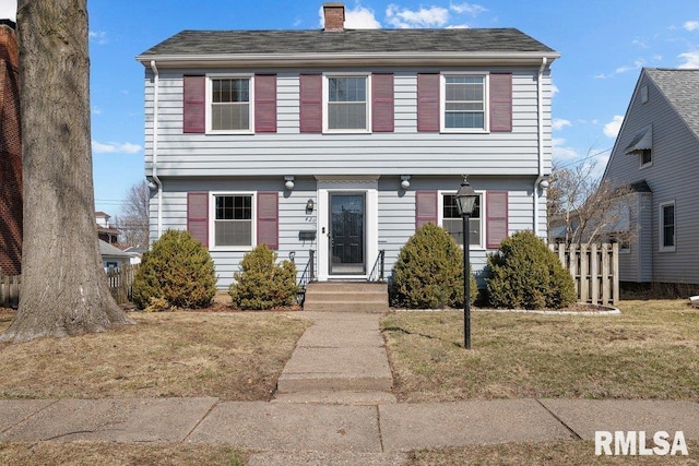 colonial inspired home featuring a chimney, a front yard, and fence