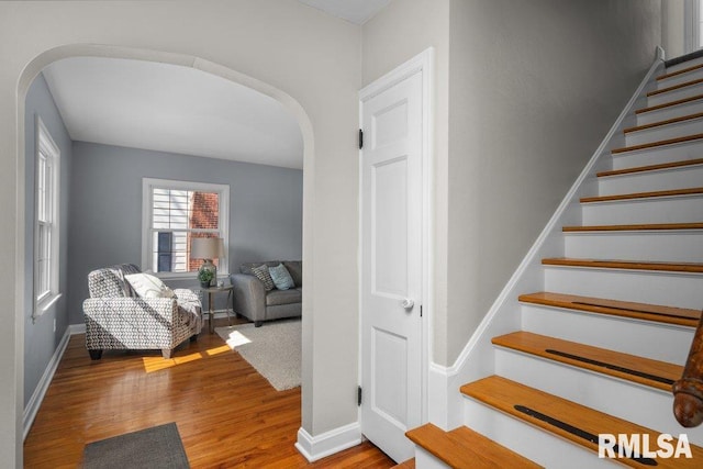 stairway featuring arched walkways, baseboards, and wood finished floors