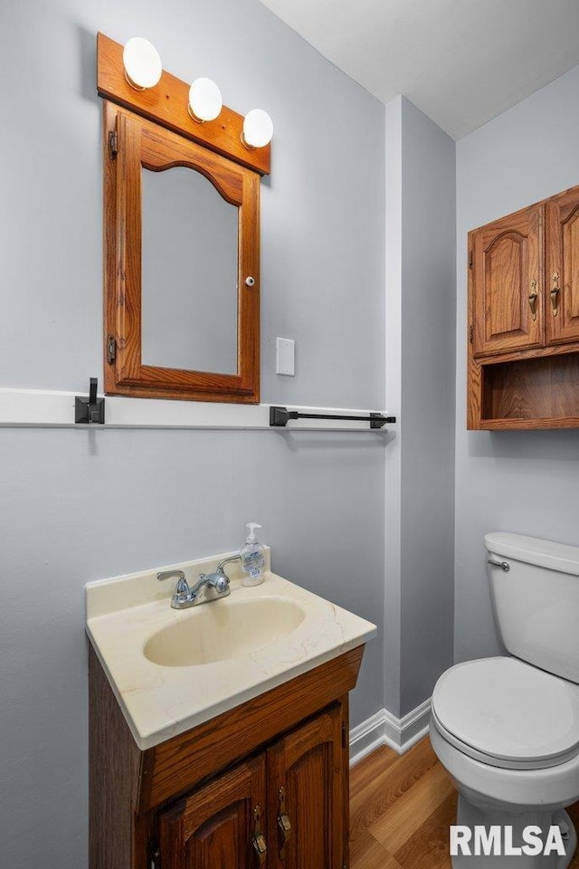 bathroom featuring baseboards, toilet, wood finished floors, and vanity