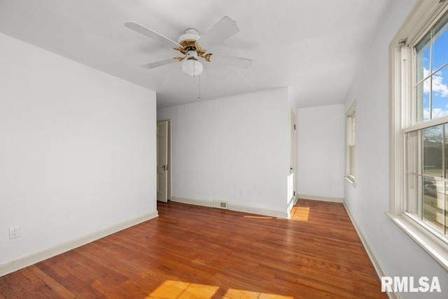 empty room with visible vents, ceiling fan, baseboards, and wood finished floors